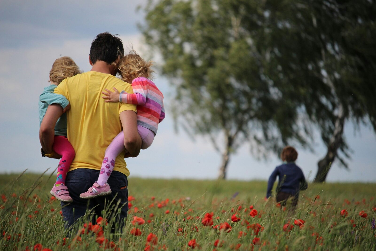 A father carrying his young children through a summer meadow